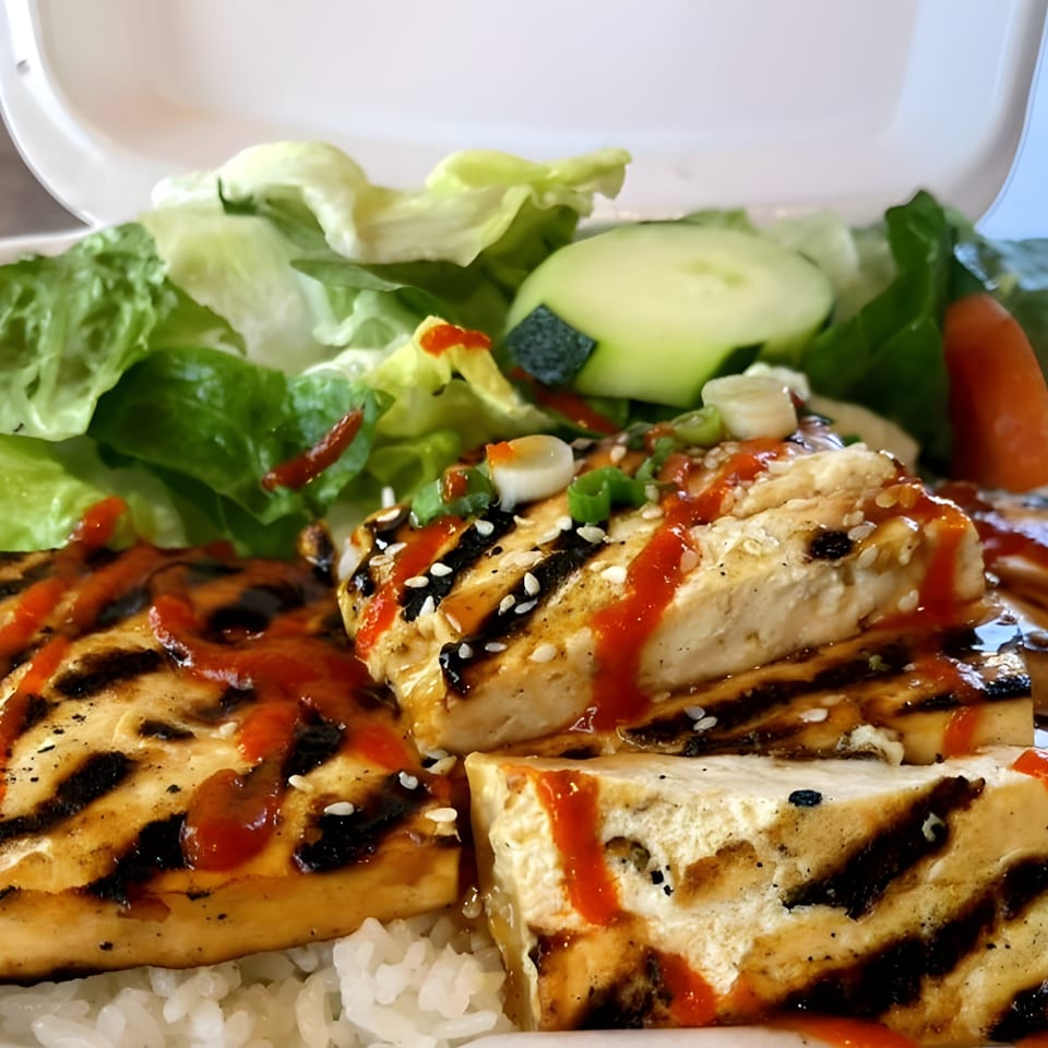 Grilled tofu with teriyaki sauce, sriracha, sesame seeds, and green onions, served with rice and salad.