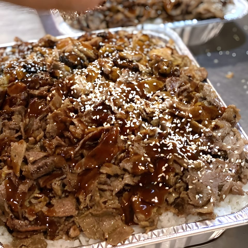 Ronin BBQ Teriyaki's beef teriyaki with sesame seeds, served over white rice in a foil container.